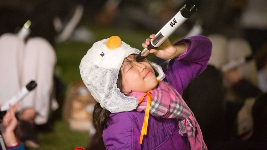 A young girl holds a telescope up to the sky.