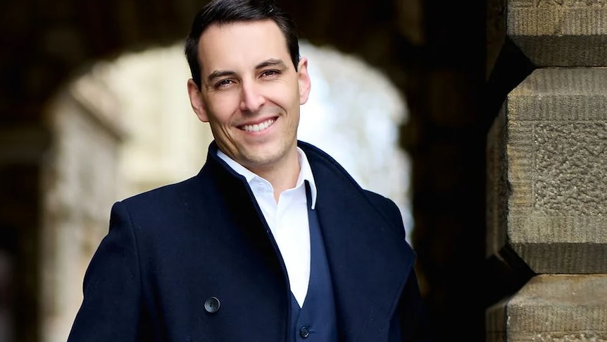 man in a blue suit and white shirt standing in front of an archway