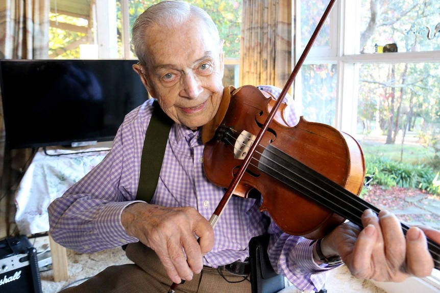 Terminally ill man, Harry Gardner, smiles at the camera as he plays his violin in his Melbourne home.