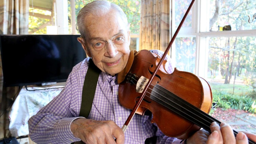 Terminally ill man, Harry Gardner, smiles at the camera as he plays his violin in his Melbourne home.