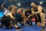 A group of Darwin wrestler squat and pose for the camera inside a gym