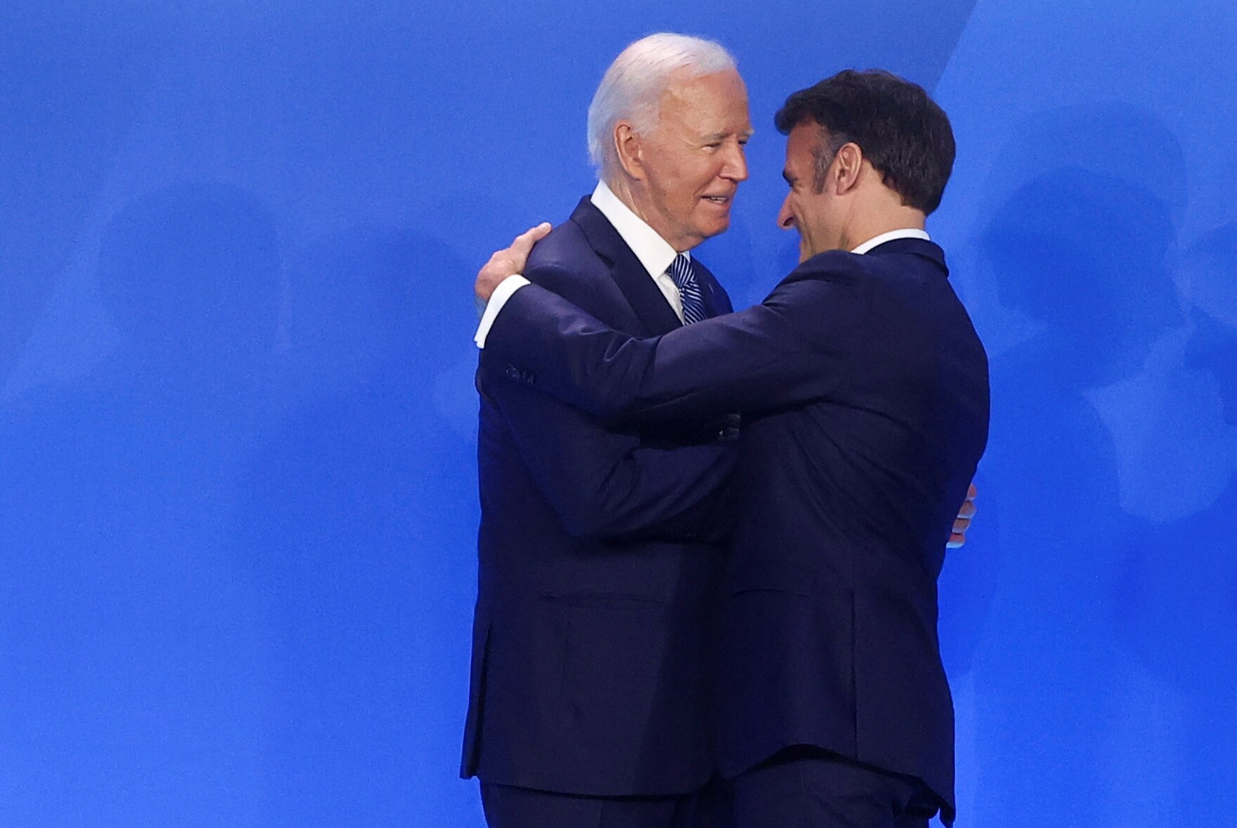 Mr Biden and Mr Macron embrace on a blue background.