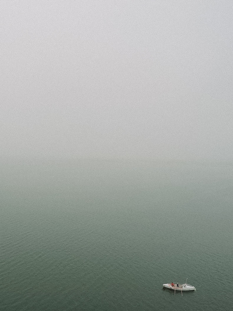 A small white boat in the right-hand corner surrounded by water and fog.