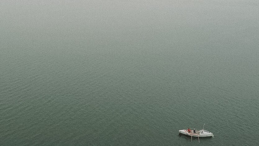 A small white boat in the right-hand corner surrounded by water and fog.