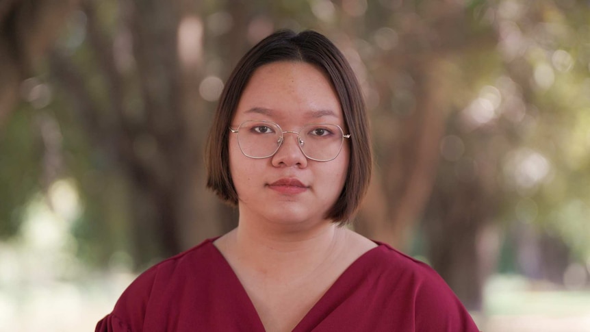 A woman with short brown hair wearing glasses and a red shirt stares at the camera.