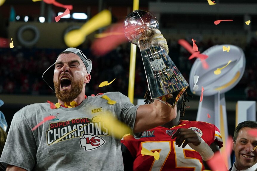 Travis Kelce shouts while holding the Vince Lombardi trophy as streamers fall after the Kansas City Chiefs' Super Bowl LIV win.