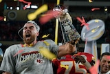 Travis Kelce shouts while holding the Vince Lombardi trophy as streamers fall after the Kansas City Chiefs' Super Bowl LIV win.
