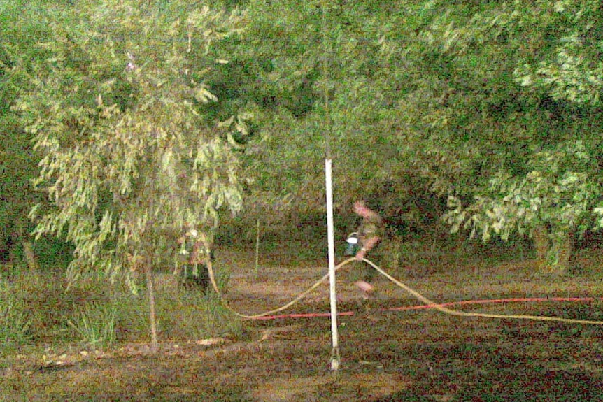 A grainy photograph showing Brendan Sokaluk carrying a hose during a bushfire