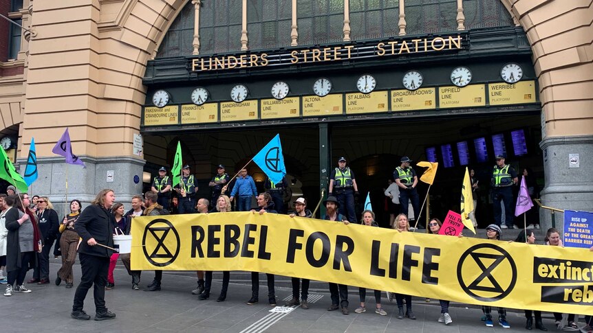 Protesters holding a banner that says rebel for life outside Flinders Street station