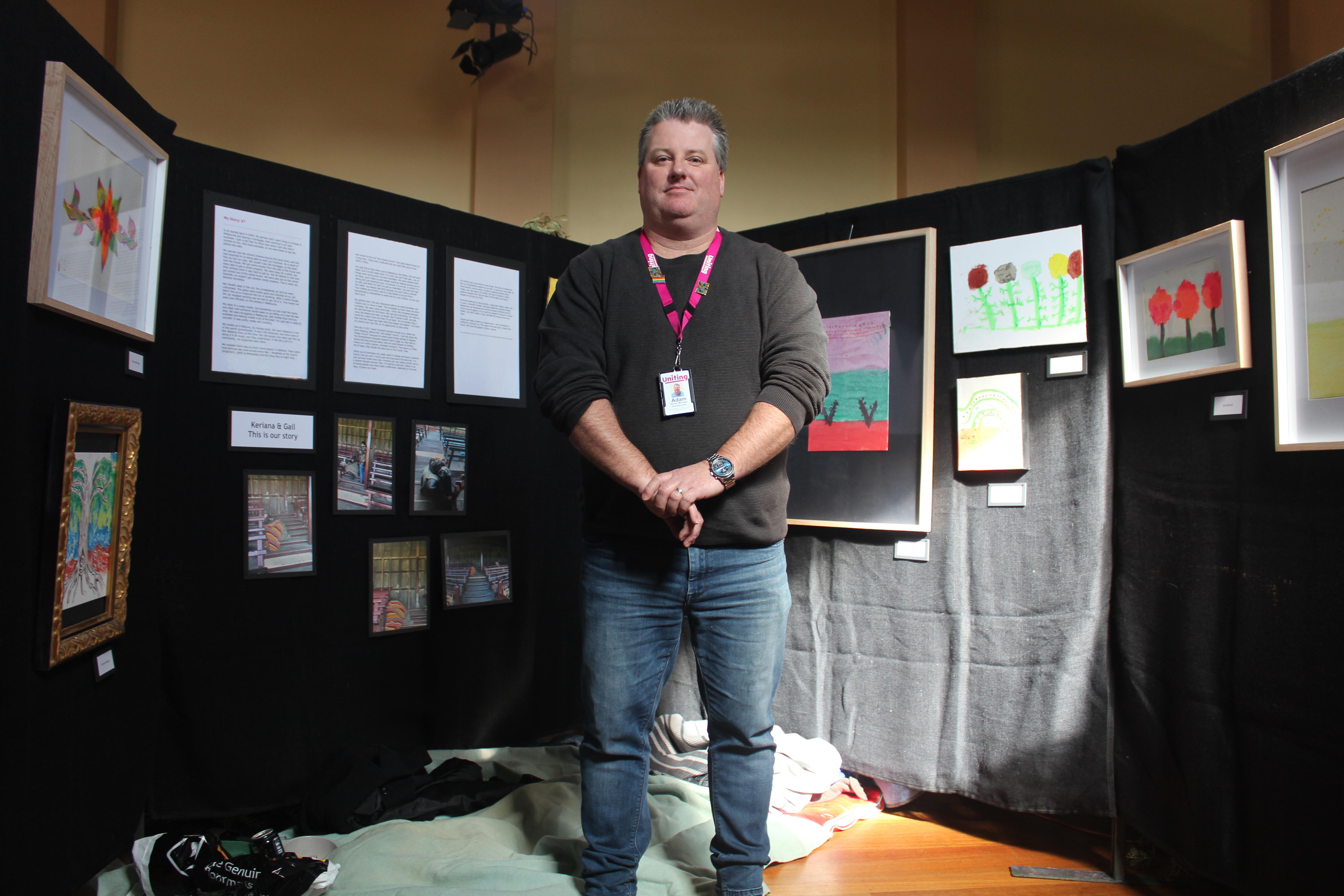 A man stands in front of artwork on a black background with his arms in front of his body, 