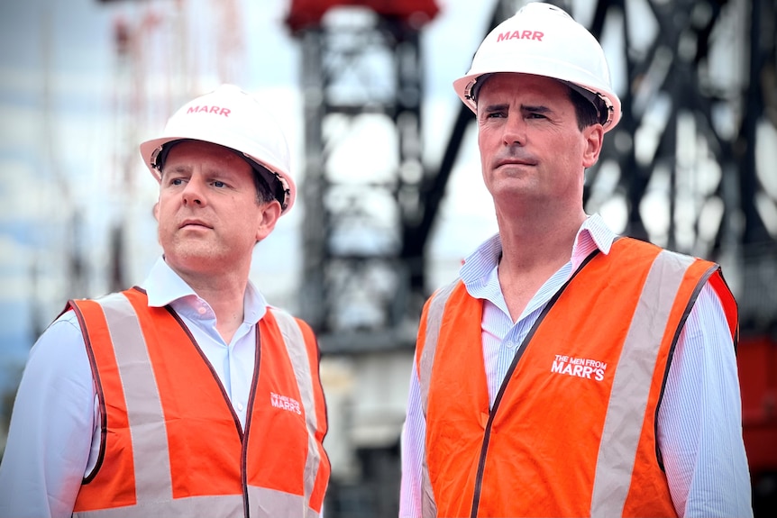 Two men wearing a white hard hat with the word 'Marr' on it and a bright orange vest stand side by side. 