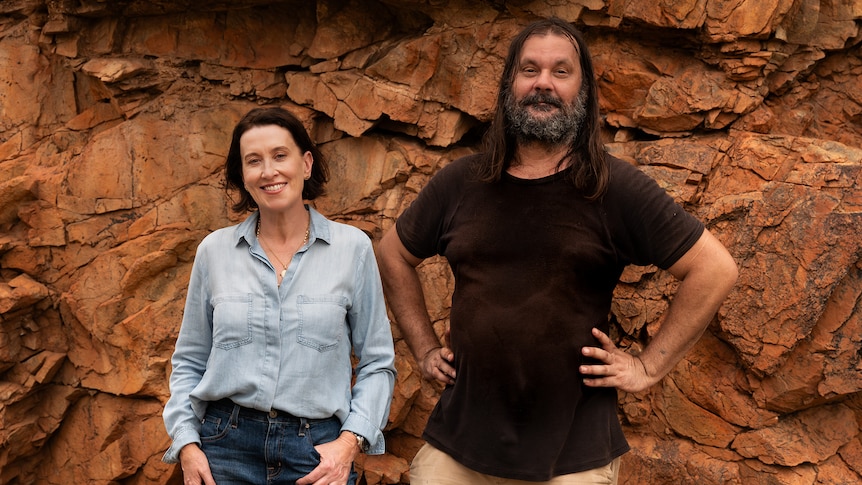 Virginia Trioli and Warwick Thornton, an Aboriginal man, stand together smiling, in front of a rock face.