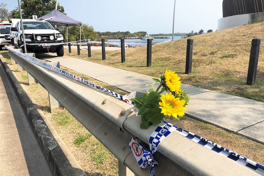 Flowers tied to a guard rail on the side of a road near some police vehicles.