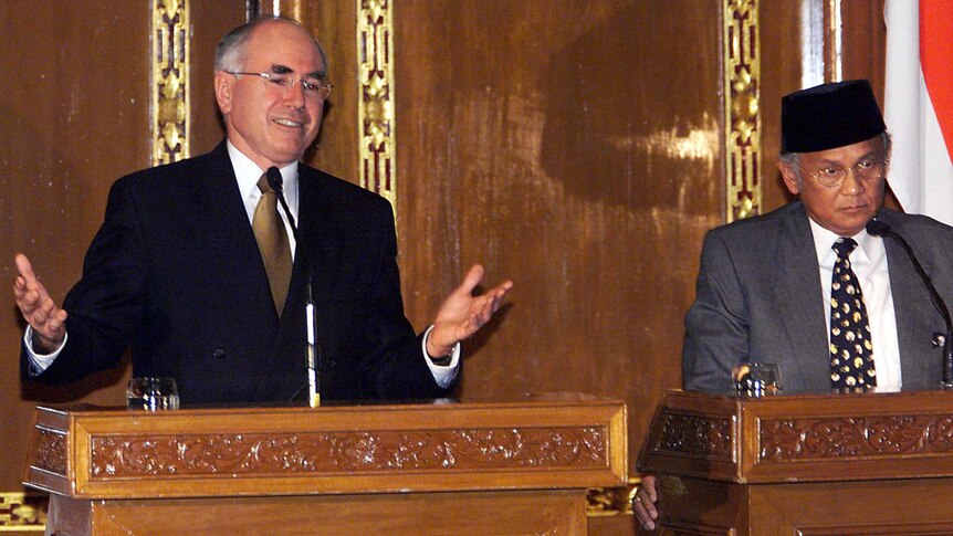 John Howard smiles a lectern, while BJ Habibie wears a serious expression.
