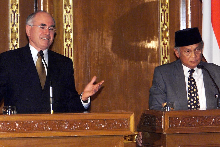 John Howard smiles a lectern, while BJ Habibie wears a serious expression.