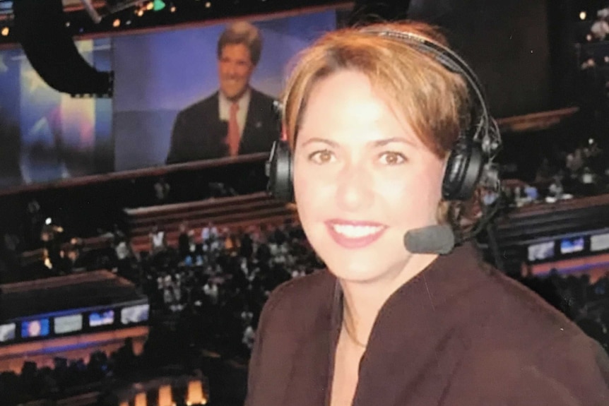 Millar with headset on and large TV with John Kerry candidate on screen in front of audience.