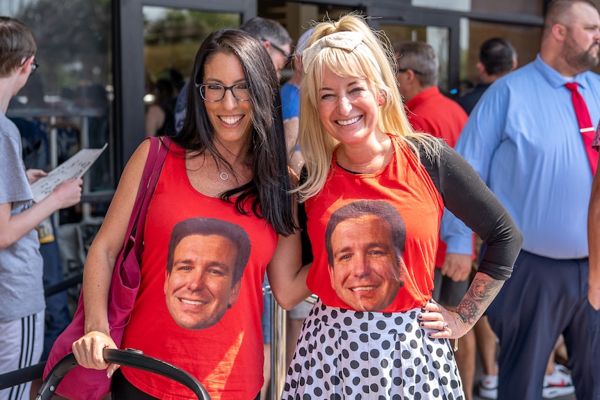 Two women wearing t-shirts with Ron DeSantis's face.