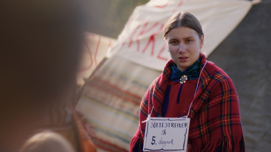 A woman in tradtional Sami clothing with a sign around her neck indicating she is on strike