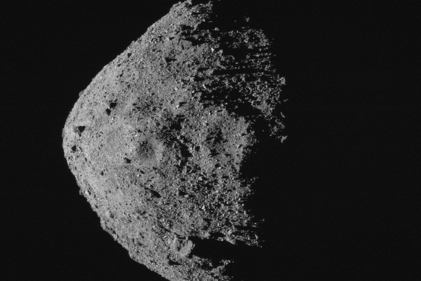 A grey asteroid is seen emerging from the darkness of space