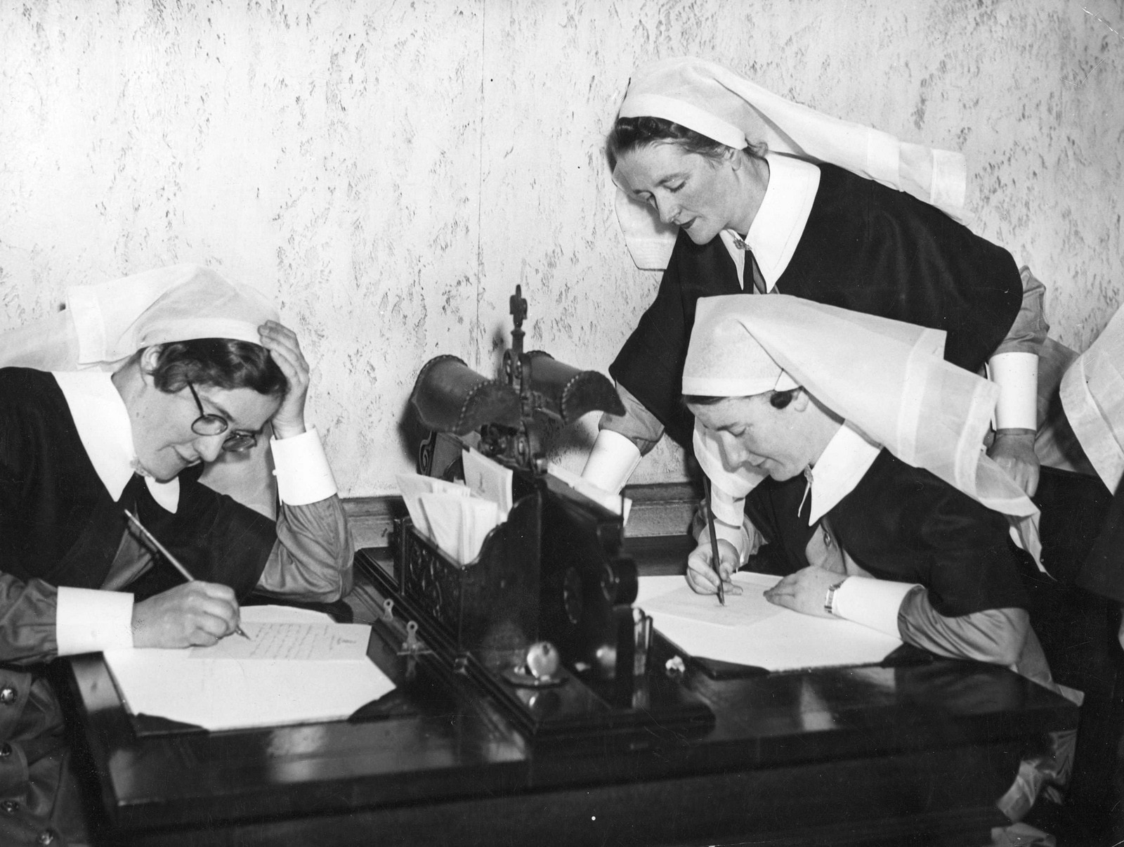 three nurses in old fashioned uniforms writing letters