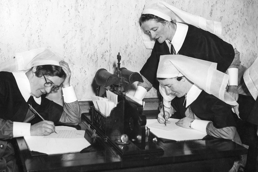 three nurses in old fashioned uniforms writing letters