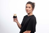 Woman with white skin and black t-shirt holds glass of dark beer standing in front of white backdrop