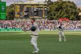 A cricketer raises his bat as he walks off Adelaide Oval with the scoreboard in the background.