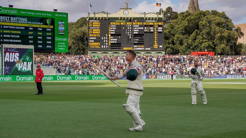 A cricketer raises his bat as he walks off Adelaide Oval with the scoreboard in the background.