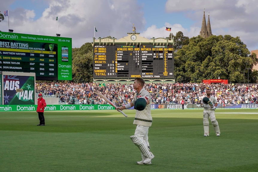 A cricketer raises his bat as he walks off Adelaide Oval with the scoreboard in the background.