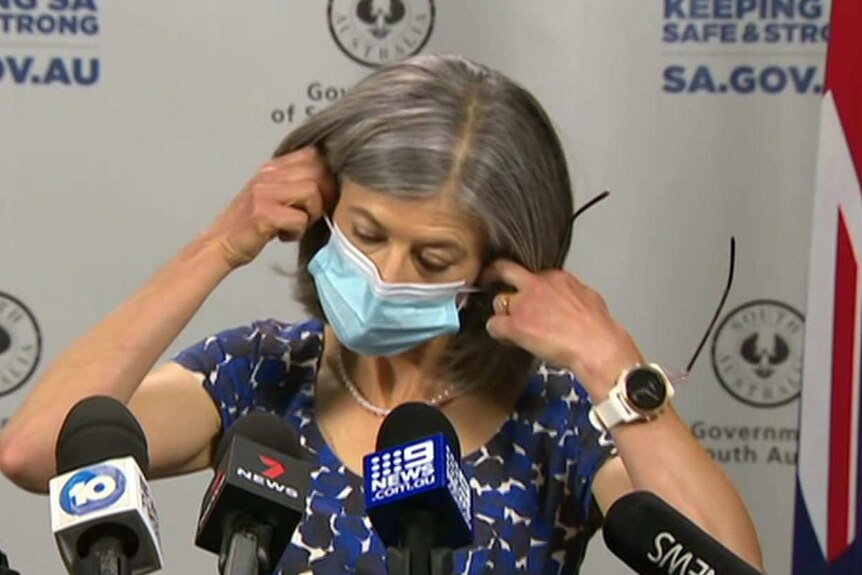 A woman with grey hair puts her hands to her ears to take off a face mask