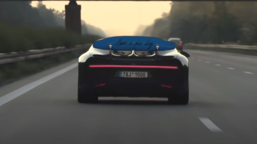 The rear wing of a Bugatti Chiron has the writing 'Have a nice day' on the back as it is driven down a road
