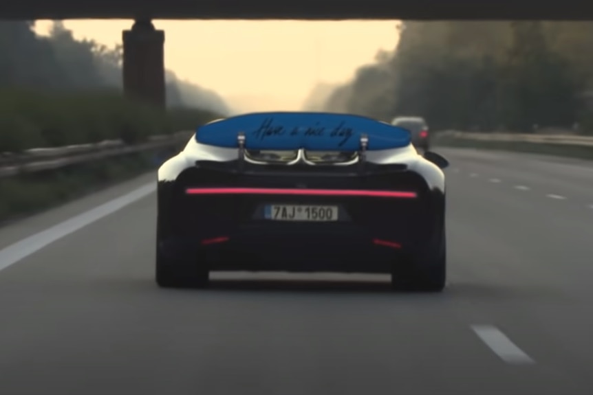 The rear wing of a Bugatti Chiron has the writing 'Have a nice day' on the back as it is driven down a road