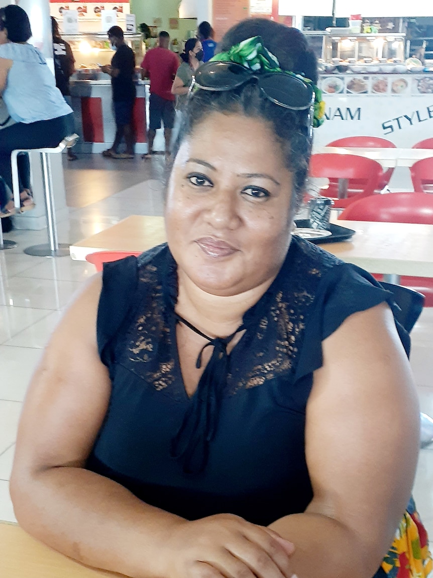 A woman with dark hair tied-back smiling from a table in a food court 