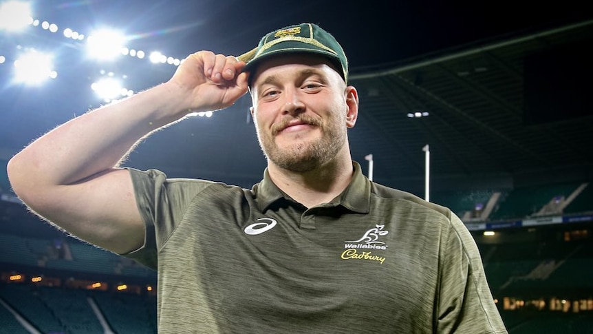 A sweaty man with a Wallabies shirt and a cap smiles at the camera