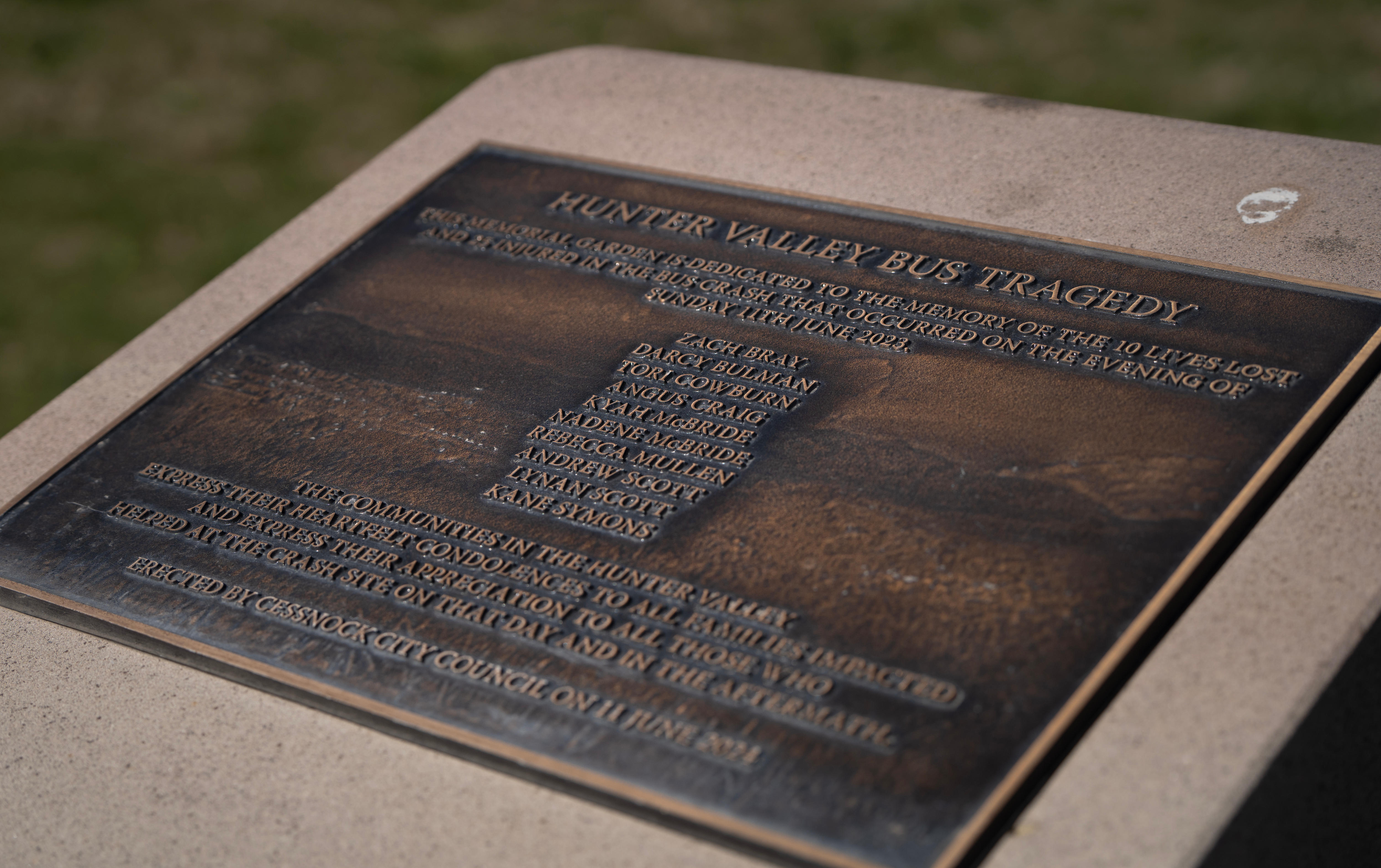 A bronze-coloured memorial plaque with blue ribbon at the base. Lists 10 people's names.