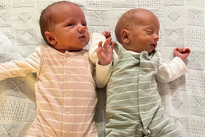 Newborn twins lie on their backs on a blanket