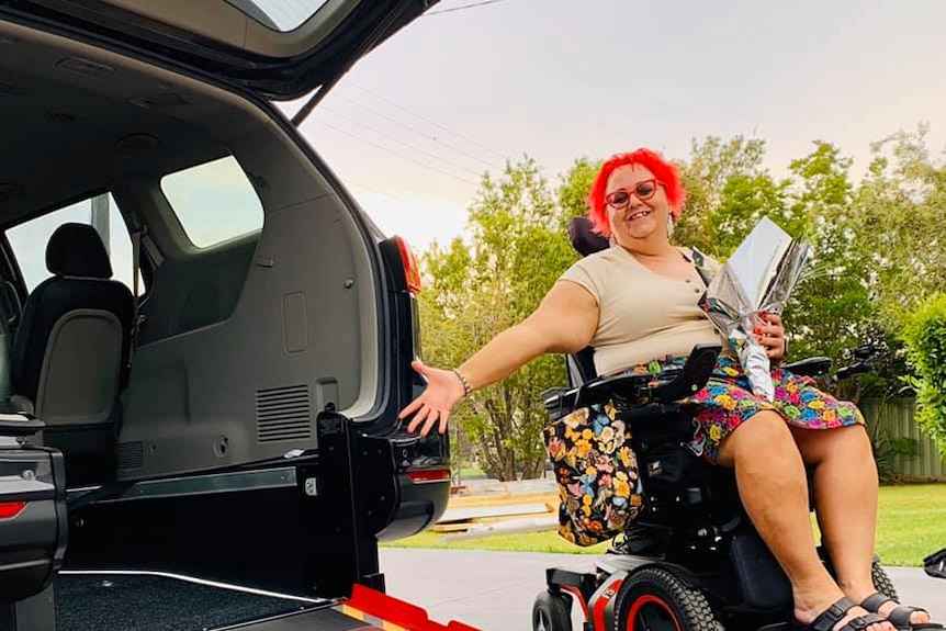 Nina Crumpton sits in her wheelchair alongside a car with a rear ramp leading into it.