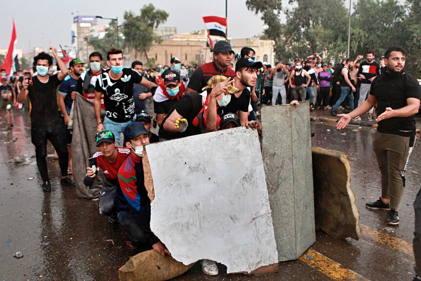 Anti-government protesters take cover while Iraq security forces fire during a demonstration in central Baghdad
