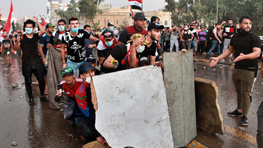 Anti-government protesters take cover while Iraq security forces fire during a demonstration in central Baghdad