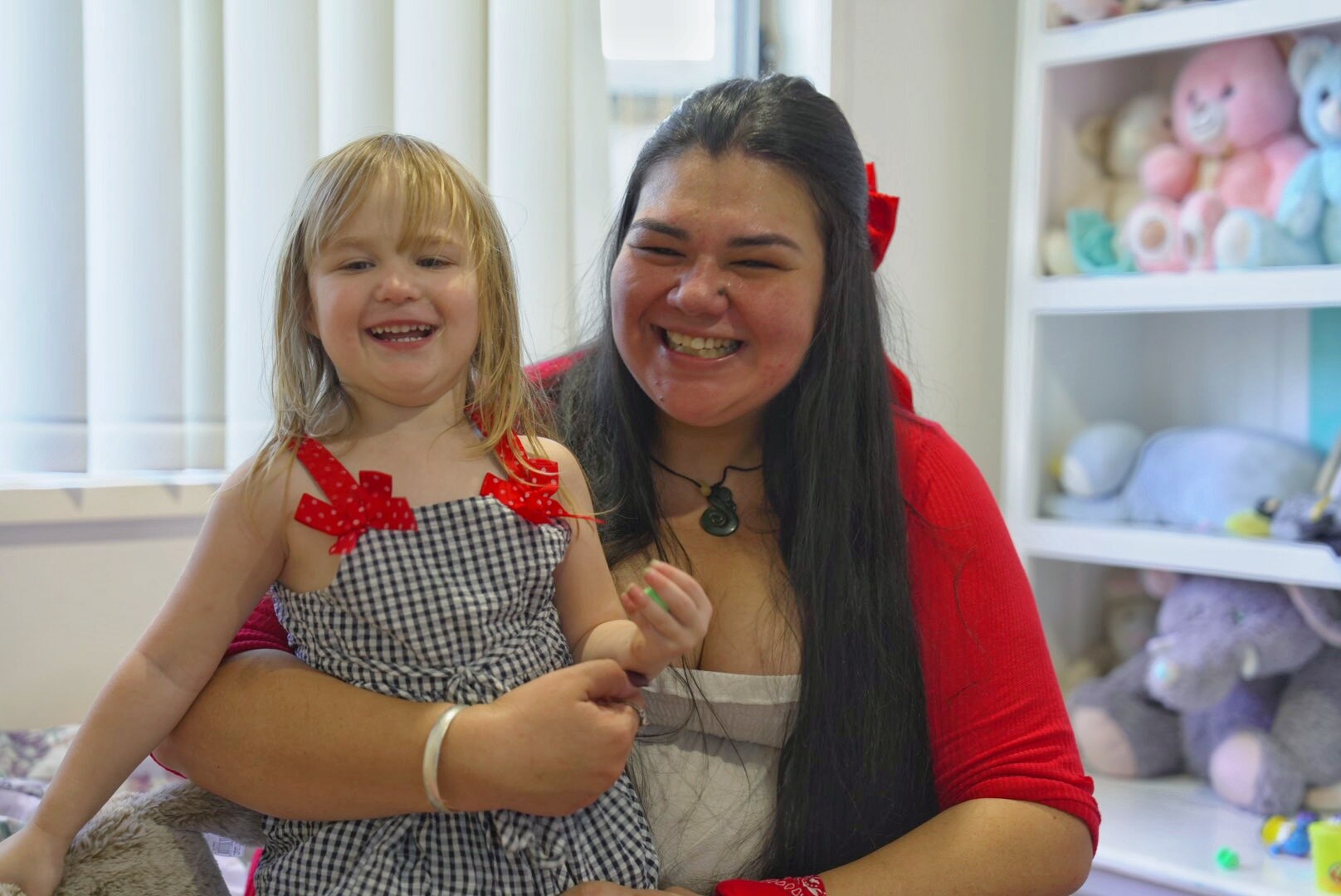 A child sits in her mother's lap on the floor and they both smile.