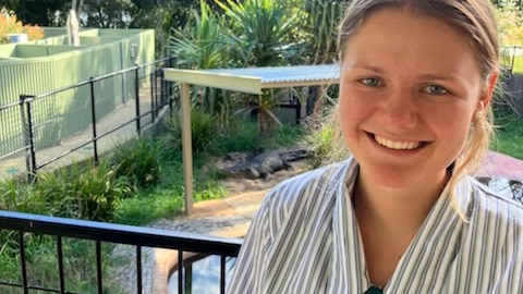 Shana Imfeld in her school uniform smiling in front of a crocodile at the zoo in Rockhampton, Queensland.