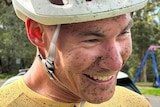 A man is smiling and wearing a helmet with splashes of mud on his face