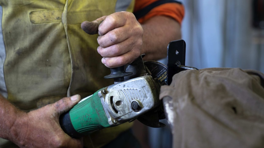 A close-up shot of a man's hands holding an angle grinder in a workshop.