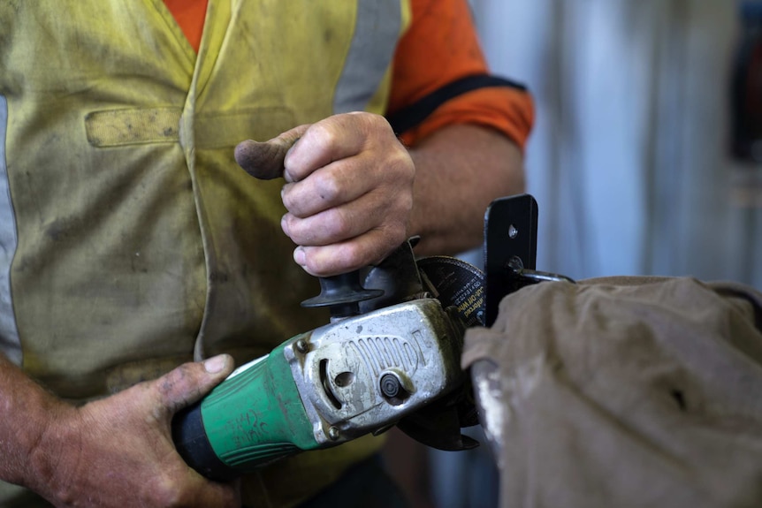 A close-up shot of a man's hands holding an angle grinder in a workshop.