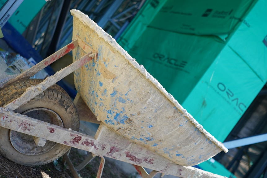 A wheelbarrow covered in dry cement in front of some Oracle bannering. 