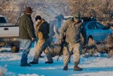 Armed militia, one holding a rifle by his side, walk through the snow in the Malheur Wildlife Refuge HQ in Oregon.