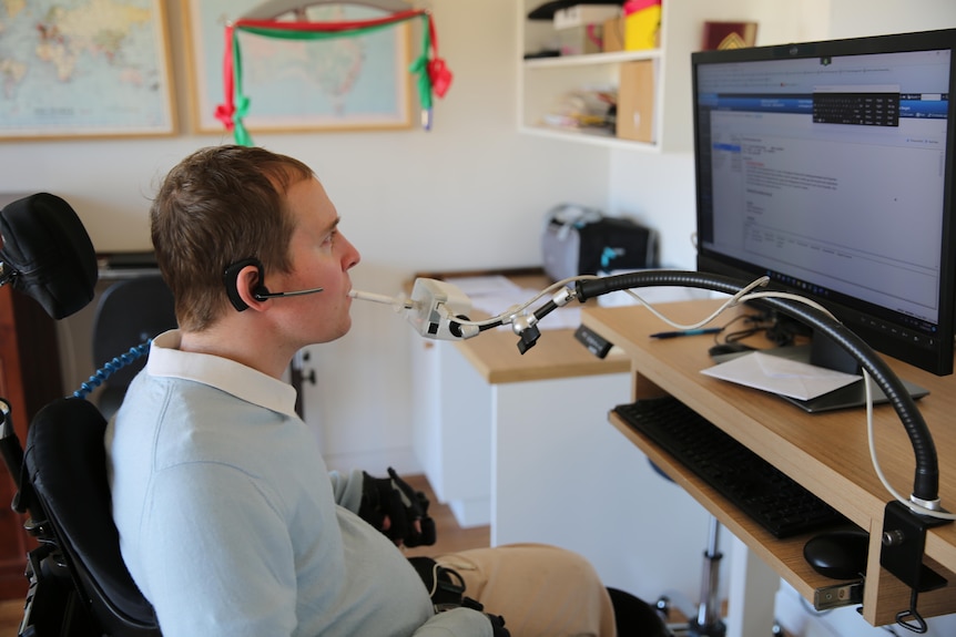 A man in a wheelchair uses a device operated by his mouth to control a computer