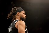 A side-on, low view of NBA player Patty Mills with a black background behind him before a Brooklyn Nets game.