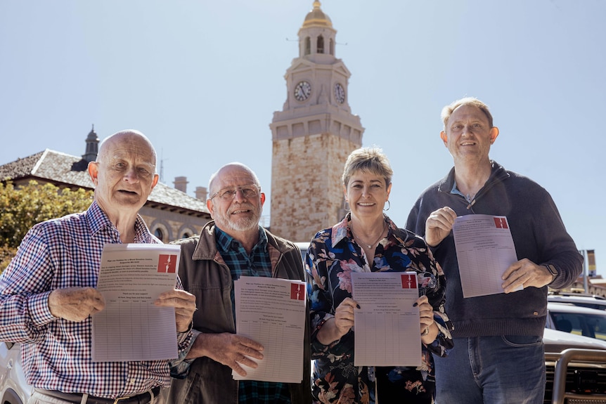 Four people display a petition while they stand in front of a historic-looking building.