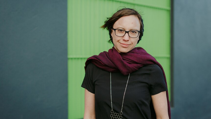 Mid-shot colour photograph of games producer Kamina Vincent standing outdoors in front of a light green and blue wall.